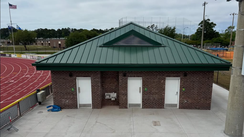 Finished brick entrance facade with green standing-seam roof and triangular roof vent at the Doug Shaw Memorial Stadium visitors support building