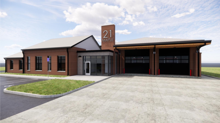 Architectural rendering of Goretown Fire Station — a red brick station with dark bay doors, a brick tower marked 21 Maple, and a glazed entrance under a clear sky